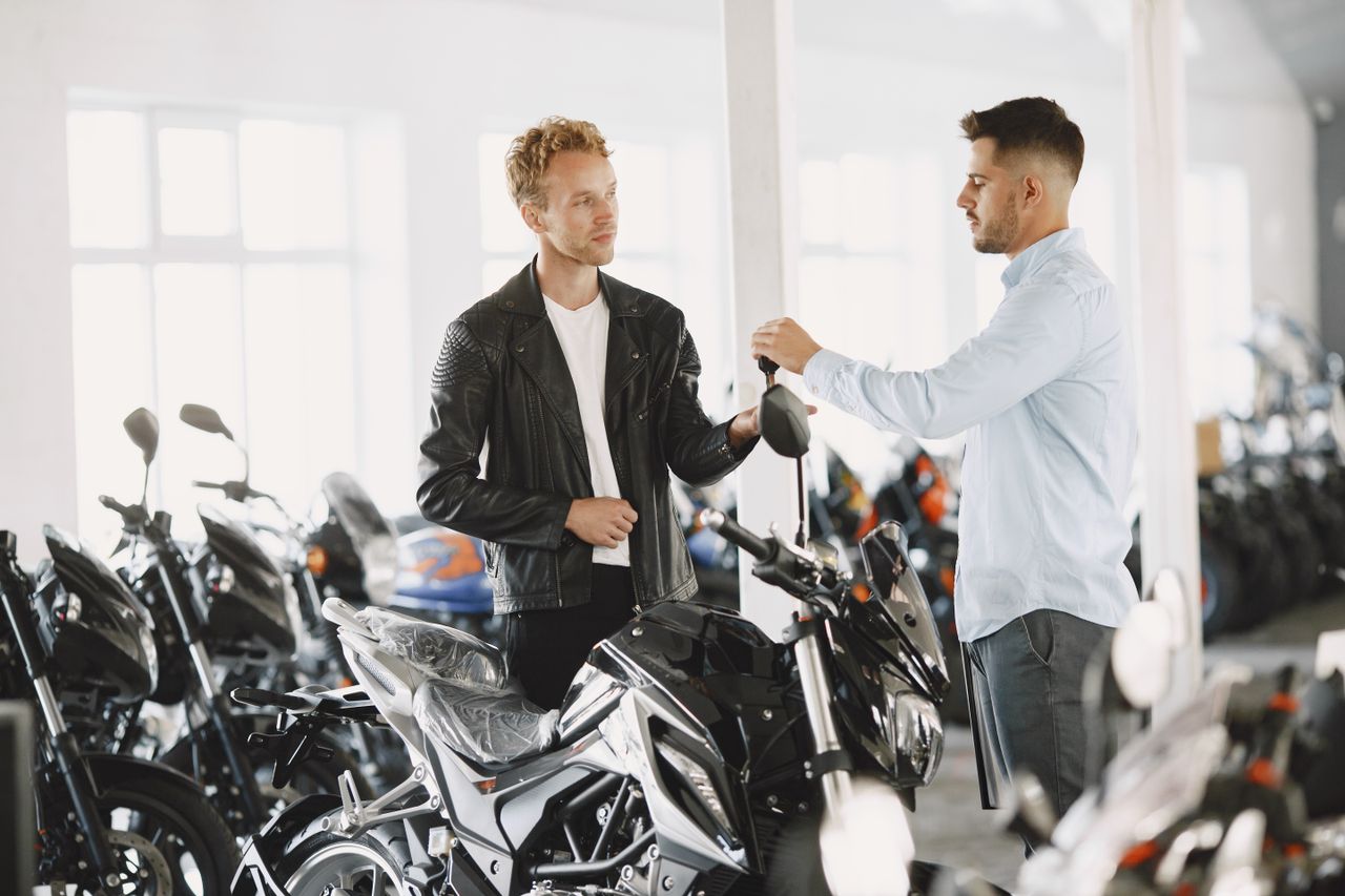 Dos personas conversan en una concesionaria de motos con varias motos nuevas alrededor